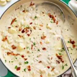 A soup pot filled with Clam Chowder with bacon and parsley on top.