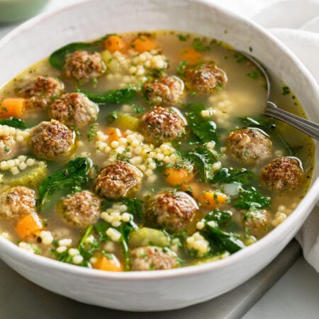 A bowl of Italian Wedding Soup in a bowl with meatballs, spinach, carrots, and pasta.